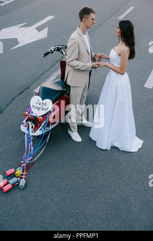 Hochzeit paar Hand in Hand auf der Straße in der Nähe von Scooter mit 'Just Married' Herz Zeichen und bunten Dosen auf Bänder Stockfoto