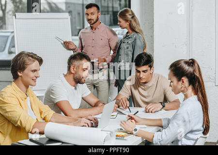 Geschäftsleute, die sich bei Tisch und in der Nähe von Flipchart im Büro Stockfoto