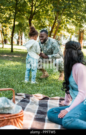 Lächelnd afrikanische amerikanische Soldaten in der Nähe der Tochter im Park hocken Stockfoto