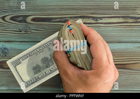 Männliche hand mit einem gefalteten Paket von 100 USD Notizen über einen rustikalen Holztisch mit einer Banknote seitlich öffnen sich in einem Overhead konzeptionelle Stockfoto