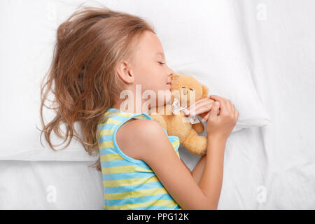 Erholsame weibliches Kind mit leichten unordentlicher Frisur, liegt seitlich, hält Ihr Favorit Teddybär in der Hand, genießt, gesunden Schlaf in der Nacht, weiche bedcl Stockfoto