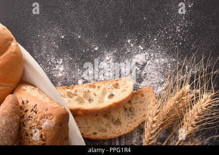 Brot auf Korb mit Tuch und schwarzer Holztisch mit Weizen und Mehl. Ansicht von oben. Horizontale Zusammensetzung Stockfoto