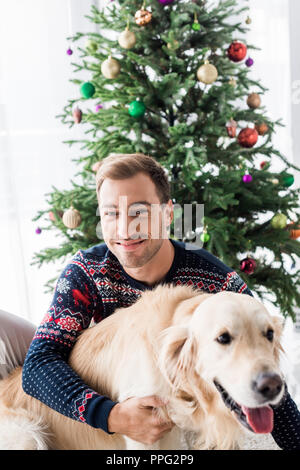 Lächelnd Mann in Weihnachten Pullover umarmen Golden Retriever Hund Stockfoto