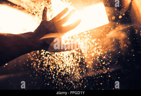 Ein Mann Hand in einem Spray von Wasser im Sonnenlicht vor einem dunklen Hintergrund. Wasser als Symbol für Reinheit und Leben. Stockfoto