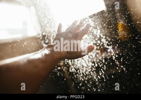 Ein Mann Hand in einem Spray von Wasser im Sonnenlicht vor einem dunklen Hintergrund. Wasser als Symbol für Reinheit und Leben. Stockfoto