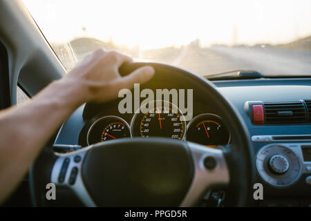 Die selektive Fokus mann Hand am Lenkrad, Auto fahren bei Sonnenuntergang. Reisen Hintergrund. Stockfoto