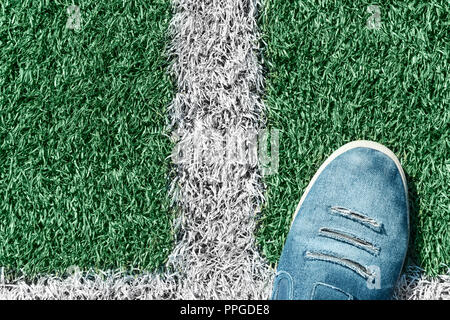 Männliche Sneaker aus zerrissenen Jeans auf einem grünen Kunstrasen Fußballplatz Stockfoto