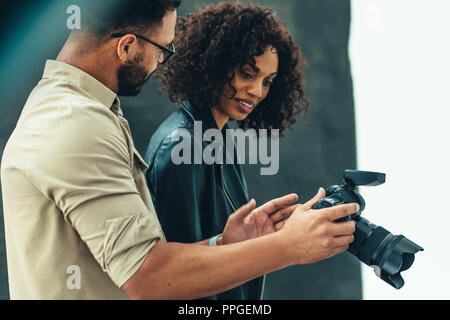 Fotograf in einem Gespräch mit einem Modell über das Fotoshooting mit der Kamera. Fotograf mit einem weiblichen Modell überprüfung Fotos während der Dreharbeiten. Stockfoto