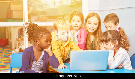 Kinder spielen zusammen am Laptop mit Erzieherin im Kindergarten Stockfoto