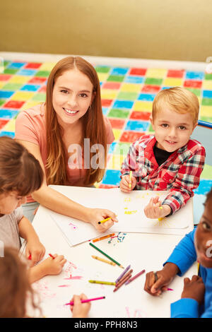 Frau als Erzieherin malt und zeichnet zusammen mit den Kindern im Kindergarten oder in der Vorschule Stockfoto
