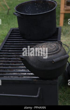 Alte schwarz Gusseisen Wasserkocher auf ein Gitter aus einem Holzofen Grill im Freien Stockfoto