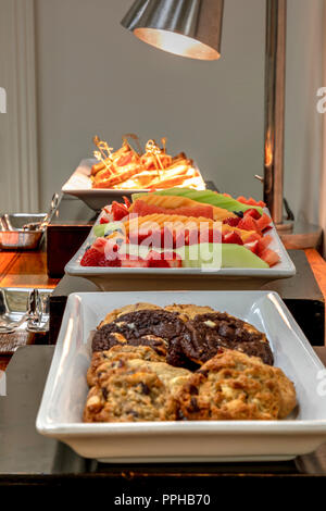 Buffet einschließlich gegrillte Reuben Sandwiches unter einer Heizung, frisches Obst, und verschiedene Cookies. Stockfoto