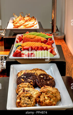 Buffet einschließlich gegrillte Reuben Sandwiches unter einer Heizung, frisches Obst, und verschiedene Cookies. Stockfoto