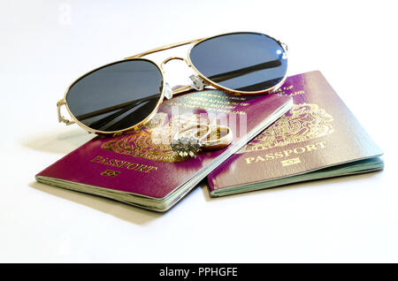 Urlaub, Reisen und Flitterwochen Konzept - ein Rot, Burgund, britischen Europäischen Pass und eine Sonnenbrille und Hochzeit Ringe auf einem weißen Hintergrund. Stockfoto