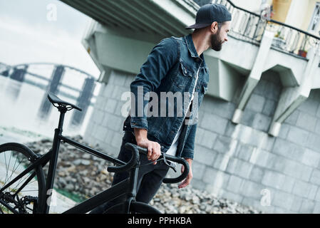 Freizeitaktivitäten im Freien. Junge stilvollen Mann auf der Straße mit dem Fahrrad beiseite schaut nachdenklich Stockfoto