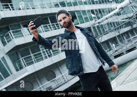 Freizeitaktivitäten im Freien. Junge stilvollen Mann auf der Straße der Stadt, die auf dem Smartphone selfie Foto lächelt glücklich Stockfoto