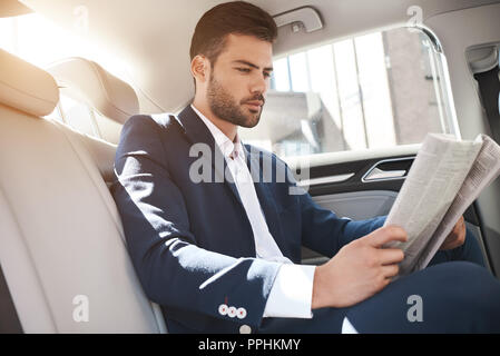 Junge stilvolle Geschäftsmann liest Zeitung auf dem Rücksitz des Autos Stockfoto