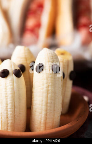 Nahaufnahme der einige Lustige Halloween Essen, wie z. B. Bananen mit den Augen als Geister oder Hotdogs in Form von blutigen Finger, auf einem rustikalen Tisch Stockfoto