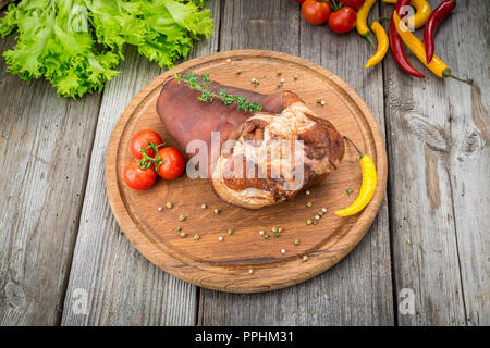 Geräucherter Schinken Hock mit Kräutern und Gewürzen auf Holzplatte. Stockfoto