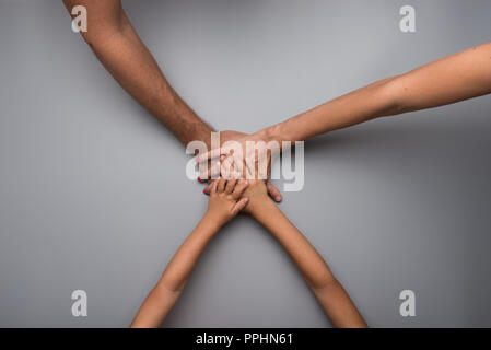 Familie, umklammern die Hände in einer Teamarbeit und Engagement Konzept mit Mama, Papa und zwei Kindern auf einem grauen Hintergrund mit kopieren. Stockfoto