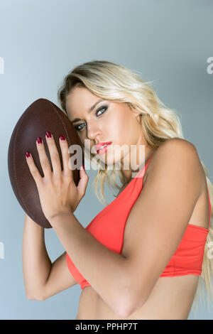 Close-up Portrait von sportliche junge Frau mit American football Ball und Kamera auf Grau Stockfoto