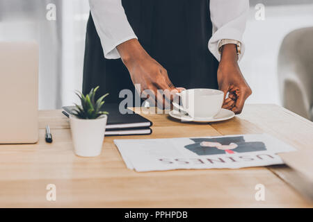 Zugeschnittenes Bild von stilvollen afrikanischen amerikanischen Geschäftsfrau, Tasse Kaffee am Tisch im Büro Stockfoto