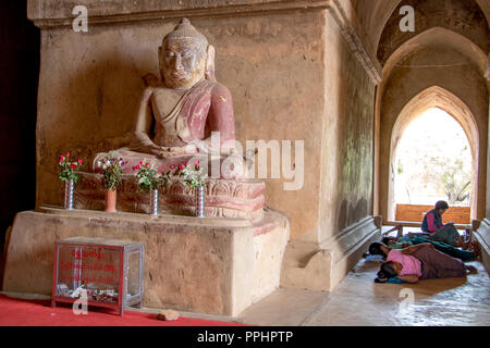 BAGAN, Myanmar, 17. Mai 2018, müde Menschen im Inneren des buddhistischen Tempel ruht mit Statue des Sitzenden Buddha, Myanmar. Stockfoto