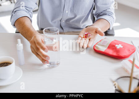 Zugeschnittenes Bild von kranken Manager holding Pillen und Glas Wasser am Tisch im Büro Stockfoto