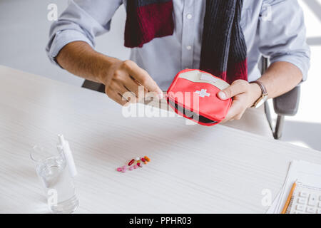 Zugeschnittenes Bild von kranken Manager im Schal öffnen Erste Hilfe Kit im Büro Stockfoto