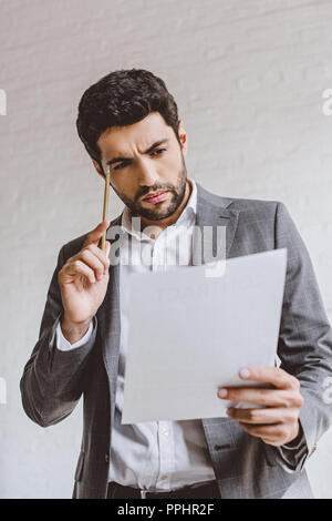 Ernsthafte Geschäftsmann Lesen von Dokumenten und berührt, Kopf mit Bleistift im Büro Stockfoto