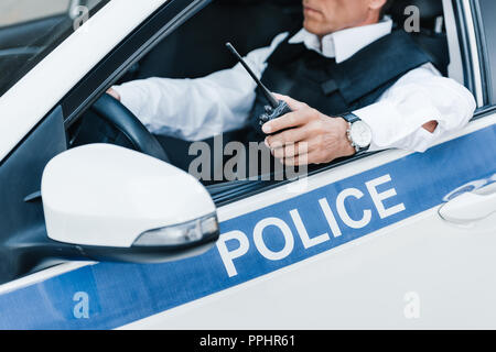 Teilweise mit Blick auf die männliche Polizisten in schusssicheren Weste Holding walkie-talkie im Auto. Stockfoto