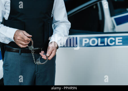 Teilweise mit Blick auf die männliche Polizisten holding Handschellen in der Nähe von Autos auf der Straße Stockfoto