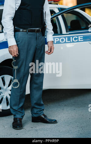 Zugeschnittenes Bild der männlichen Polizisten holding Handschellen in der Nähe von Autos auf der Straße Stockfoto