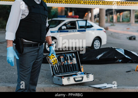 Teilweise mit Blick auf die Polizisten in Latex Handschuhe halten Polizei am Tatort mit Leiche in body bag Stockfoto