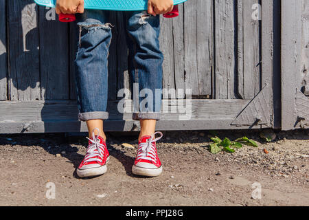 Close up Füße eines Mädchens in rote Turnschuhe und Blue Penny Skate Board mit rosa Räder neben der Wand stehen. Städtische Szene, Leben in der Stadt. Sport, Fitness Stockfoto