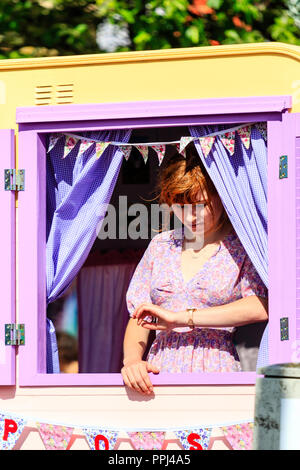 Junge kaukasier teeange Frau in lila Kleid, stehend im malerischen lila Fensterrahmen, während sie an ihrer Taille Watch suchen. Stockfoto