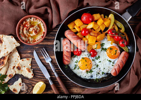 Ansicht von oben auf eine Pfanne mit Spiegelei, Ahorn verglast, Kürbis, Paprika, Tomaten, gebratene Würstchen mit lecker dip Baba ganoush, cayenne Peppe Stockfoto