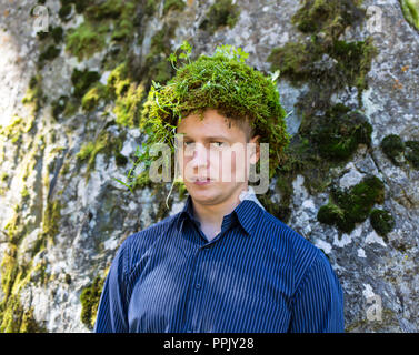 Büroangestellter in einen Anzug, im Freien mit einem Make-up im Gesicht und Moos auf seinem Kopf. Der Mensch verschmilzt mit der Natur Stockfoto