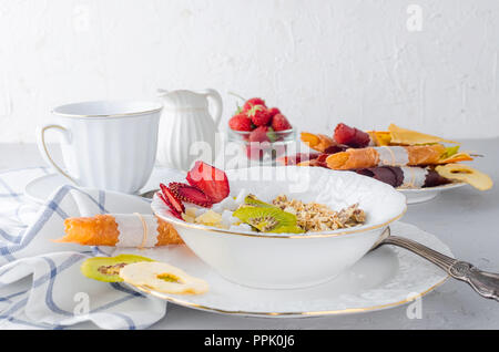 Hausgemachtes Müsli mit Haferflocken, Nüsse und getrocknete Früchte in einem weißen Teller und Tasse Kaffee auf weißem Beton Hintergrund, selektiver Fokus Stockfoto