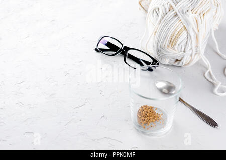 Glas mit Kaffee Korn, weiß stricken Threads und glasseson auf weißem Beton strukturierte Tabelle, selektiver Fokus, Kopieren, Ansicht von oben, Stockfoto