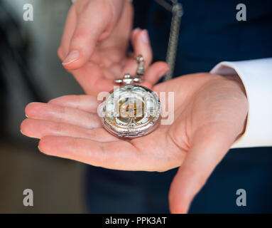 Männliche Bräutigam Hände Anzeige einer modernen, silbernen durchbohrt vorne Taschenuhr auf seiner Hand mit weißen Ärmeln angezeigt Stockfoto