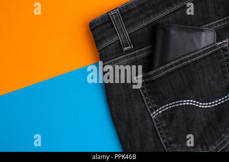 Tasche auf der Rückseite der schwarzen Jeans und schwarzem Leder Brieftasche auf orange und blau hintergrund Stockfoto