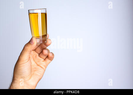 Die Hand eines Mannes hält ein Glas mit Flüssigkeit auf einem grauen Hintergrund Stockfoto