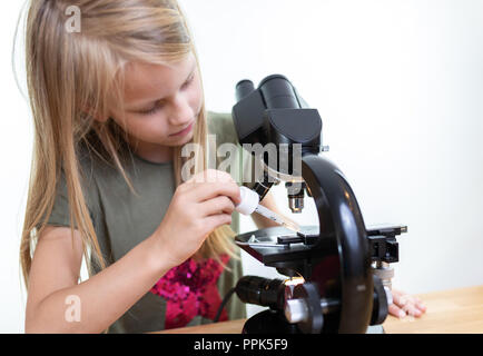 Porträt eines 7-jährigen Mädchens Tropfen Flüssigkeit auf die Oberfläche eines Mikroskops mit einer Pipette. Vor weißem Hintergrund, Stockfoto