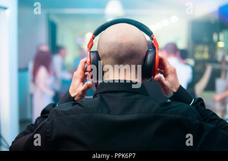 DJ mit roten Kopfhörer bei Nacht Party unter dem weißen Licht und Leute im Hintergrund. Charismatische disc jockey an der Drehscheibe. Stockfoto