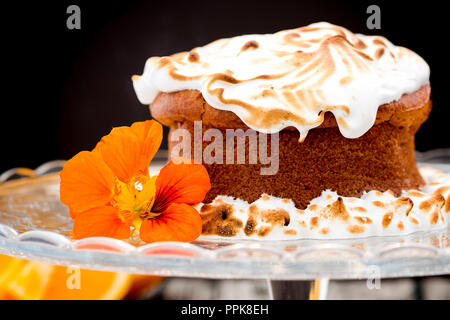 Ganze orange Kuchen mit Baiser topping und essbaren Blüten Stockfoto