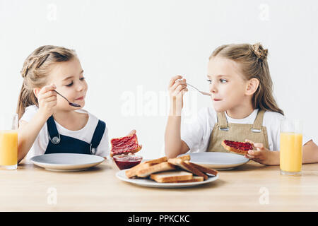 Adorable kleinen Schwestern essen Toast mit Marmelade zum Frühstück isoliert auf weißem Stockfoto