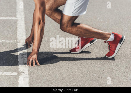 Zugeschnittenes Bild der männlichen Sprinter in Grundstellung auf der Laufstrecke Stockfoto