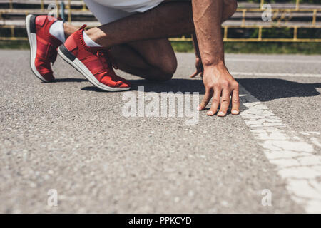 Zugeschnittenes Bild der männlichen Sprinter in Grundstellung auf der Laufstrecke Stockfoto