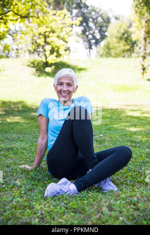 Ältere Frau Sitzen und Ausruhen nach Training im Park Stockfoto